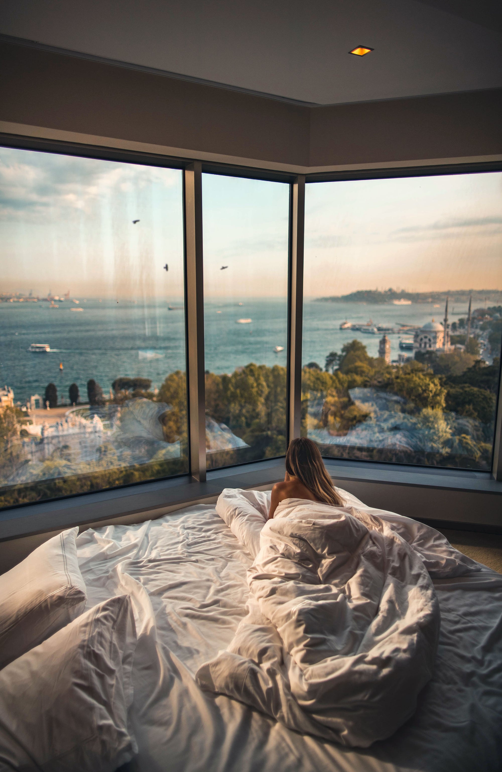 Girl in bed wrapped in a comforter looking at the view of the sea